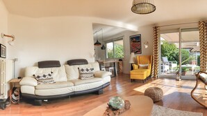 A spacious living room with a sofa, yellow armchair, and a rocking chair. There is a dining area with a table and chairs visible through an open door. - Quiet house + T2, garden & Spa, close to beaches (Anglet)