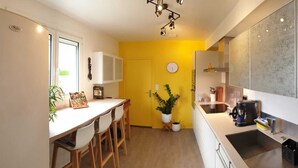 A compact kitchen with a yellow accent wall, a dining area with a table and chairs, and a coffee machine. - Quiet house + T2, garden & Spa, close to beaches (Anglet)