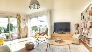 A modern living room with a sofa, a coffee table, a television, and a bookshelf. - Quiet house + T2, garden & Spa, close to beaches (Anglet)