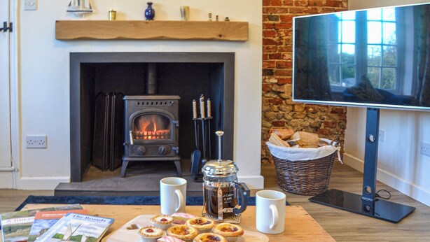 Una sala de estar acogedora con chimenea, televisor y una mesa con pasteles y libros.