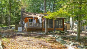 Een chalet met een houten terras, schoorsteen en veranda.