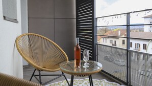 Ein Balkon mit Korbstühlen, einem Glastisch, einer Flasche und einem Glas.