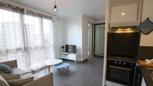 Ein modernes Wohnzimmer mit einer Couch, einem kleinen runden Tisch und einem Fernseher. Es gibt eine Küchenzeile mit einem Herd und einer Mikrowelle.