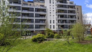 Ein mehrstöckiges Wohngebäude mit Balkonen, einer flachen Dachterrasse und einem Garten mit Rasen und kleinen Pflanzen.