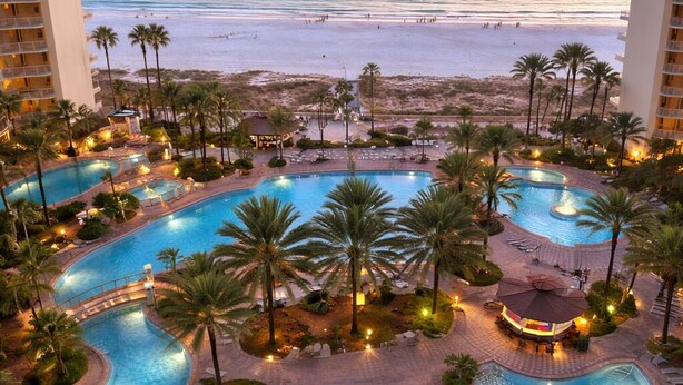 A resort with multiple swimming pools, palm trees, and a beach view.