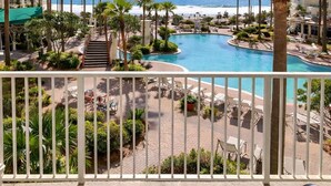 A resort pool with palm trees, a beach view, and a balcony with chairs.