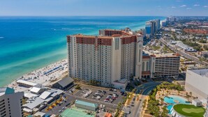 A high-rise hotel with multiple floors, a parking lot, and a beach view.