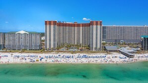 A beachfront hotel with multiple high-rise buildings, a sandy beach with numerous umbrellas, and a clear blue sky.