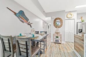 Een eetgedeelte met een houten tafel en stoelen, een decoratieve wandversiering en een houten dressoir met een spiegel.