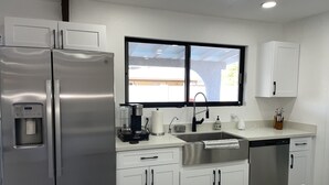 Une cuisine moderne équipée d’un réfrigérateur en acier inoxydable, d’une machine à café, d’un évier et de meubles blancs.