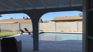 Un espace extérieur abrité comprenant une piscine, des chaises longues et un sol en béton.