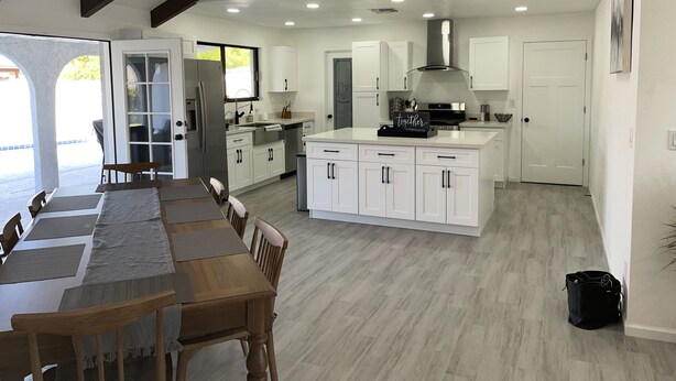 Une cuisine moderne avec des meubles blancs, un îlot central et un coin repas comprenant une longue table en bois et des chaises.