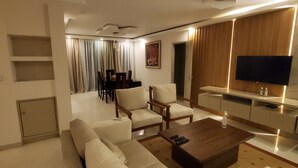 Un salon moderne avec un canapé, une table basse et un téléviseur. On aperçoit à l’arrière-plan un coin repas avec des chaises et une table.