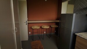 Une cuisine de taille réduite, équipée d’un réfrigérateur, de trois tabourets, d’un tapis marron et d’un comptoir en bois.