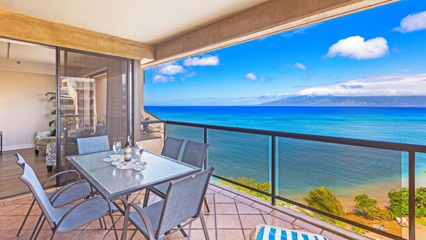 A balcony with a table and chairs, overlooking a clear blue sea and distant mountains. - UPGRADED-Sands of Kahana #275 OCEANFRONT, 3 Bed Rooms, sleeps 10 - Central AC (Lahaina)