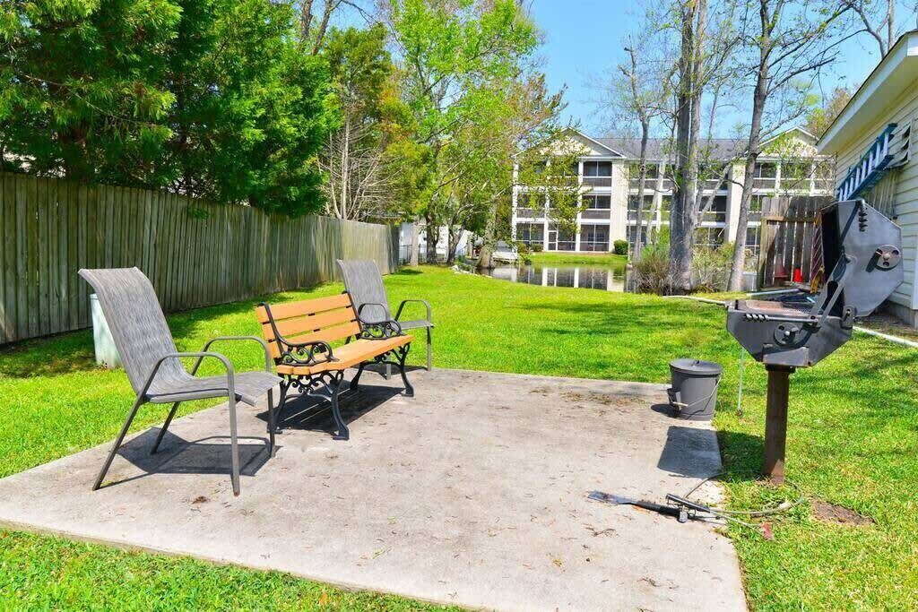 A backyard with a concrete patio, two metal chairs, a wooden bench, a barbecue grill, and a wooden fence.