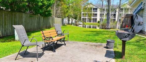 A backyard with a concrete patio, two metal chairs, a wooden bench, a barbecue grill, and a wooden fence.