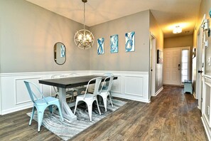 A dining area with a dark wooden table, white chairs, a patterned rug, and wall art. - Upscale Beach Retreat w Pool (North Myrtle Beach)