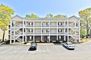 A multi-story motel with a central courtyard, two-story balconies, and a parking lot. - Upscale Beach Retreat w Pool (North Myrtle Beach)