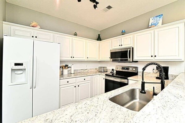A kitchen with white cabinets, a stainless steel sink, a refrigerator, a microwave, and a stove. - Upscale Beach Retreat w Pool (North Myrtle Beach)
