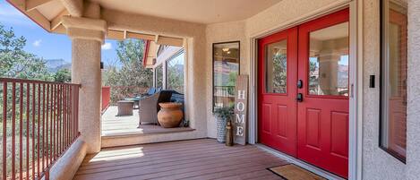 A covered porch with a red door, a small outdoor seating area with wicker furniture, and a view of the surrounding landscape.