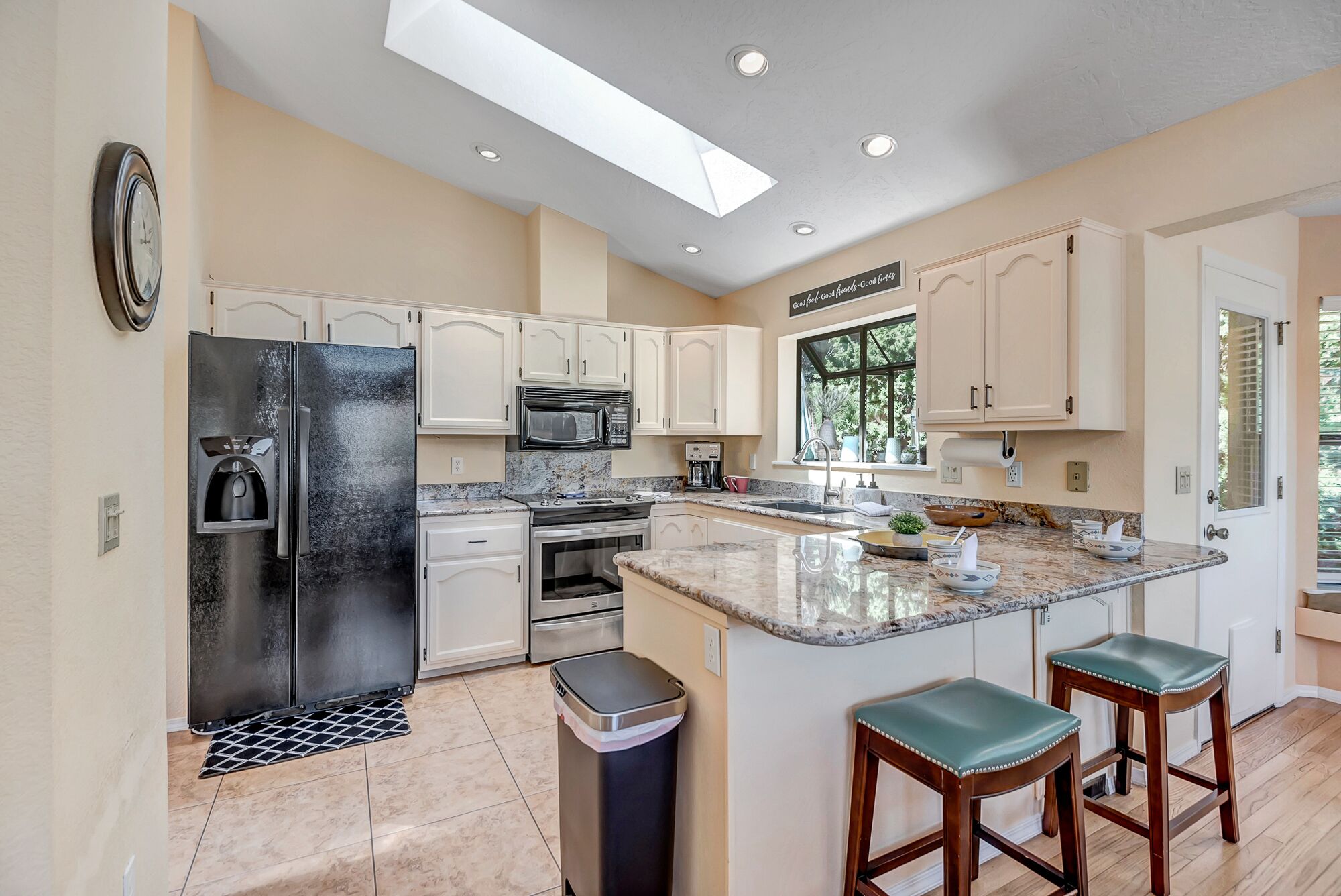 A modern kitchen with white cabinets, stainless steel appliances, a large island with stools, and a skylight.