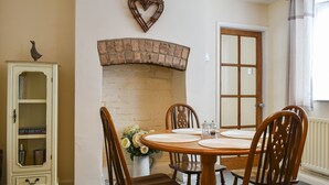 Een eethoek met een schouw van baksteen, houten stoelen, een ronde tafel en een kast met glazen deuren.