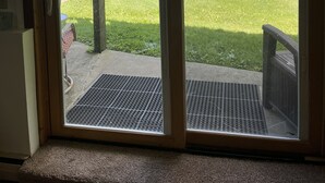 Blick aus einem Zimmer durch eine Glastür auf einen grünen Hof mit einem See und einem Schuppen.