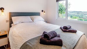 Un letto rifatto con cuscini e coperta, un comodino con un bicchiere e una finestra vista verde.