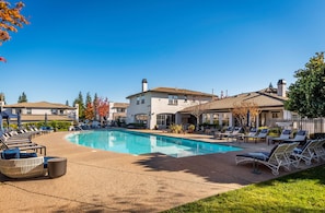 A swimming pool with lounge chairs and umbrellas, surrounded by buildings with a Mediterranean architectural style. - King Bed / Prime Location / Private Garage (Roseville)