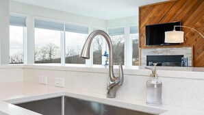 Een moderne keuken met een roestvrijstalen spoelbak, een houten wandpaneel en een raam met uitzicht op bomen.