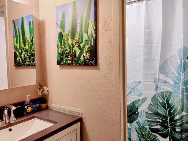 A bathroom with a sink, mirror, and two framed pictures of tropical plants. - Close to Convention Center & shops with Pool /WiFi (Honolulu)