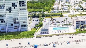 Un hotel frente a la playa con piscina, varios pisos y un puerto deportivo al fondo.