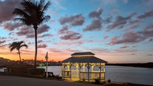 Ein Pavillon am Wasser mit Palmen und einem Sonnenuntergangshimmel.