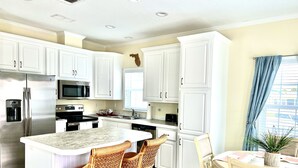Una cocina moderna con armarios blancos, electrodomésticos de acero inoxidable y una isla central con taburetes de bar.