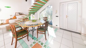 A dining area with a round table, chairs, and a staircase with green steps. - Villa Stefania - Entire Villa (Barano D'ischia)