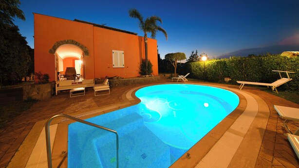 A swimming pool with a curved edge, a lounge area with chairs and a table, and a building with an arched entrance. - Villa Stefania - Entire Villa (Barano D'ischia)