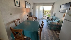 Een ruimtelijk ingerichte leefruimte met een eettafel, stoelen, een bank en een koelkast.