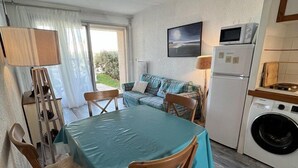 Een gezellige, compacte leefruimte met een eettafel, stoelen, een bank, een wasmachine en een magnetron.