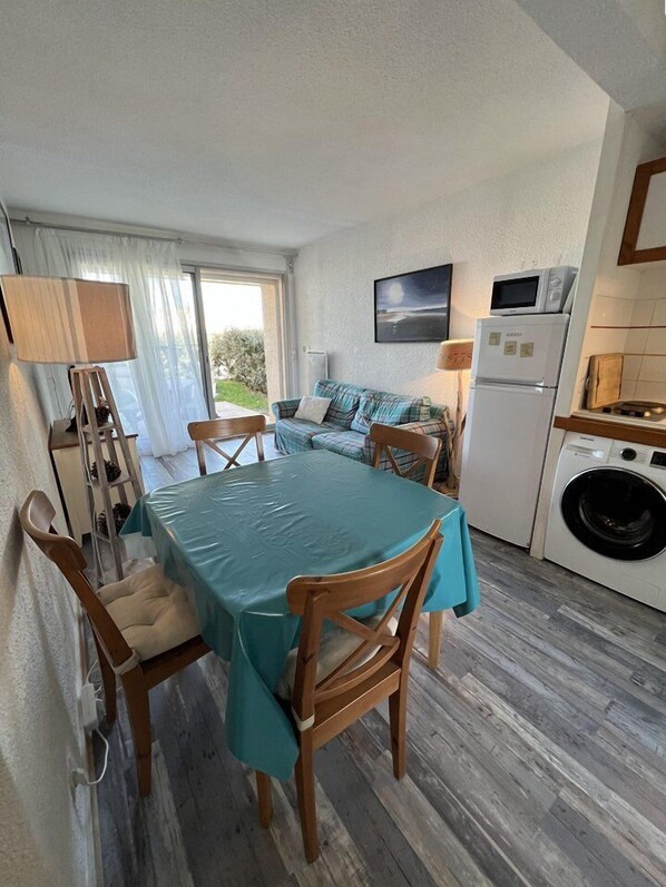 A compact living space with a dining table, chairs, a sofa, a washing machine, and a microwave.