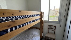 Een kleine kamer met een stapelbed, een stoel en een raam.