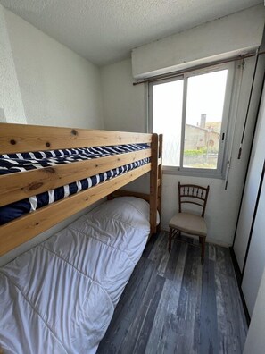 A small room with a bunk bed, a chair, and a window.