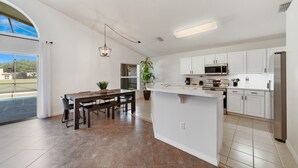 Una cocina moderna con armarios blancos, una isla central y un comedor con mesa y sillas.