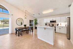 Une cuisine moderne avec des meubles blancs, un îlot central et un coin repas comprenant une table ronde et des bancs.