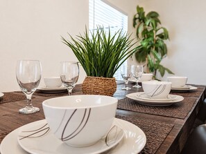 A dining table set with white plates, bowls, and wine glasses, accompanied by a woven basket and a potted plant. - 4BR Pool Home 15 min to Disney • Heated Pool & Spa • Game Room (Kissimmee)