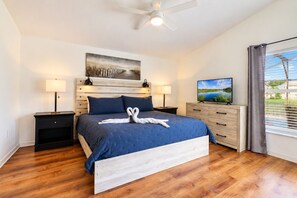 Une chambre d’hôtel avec un lit, deux tables de chevet, une télévision, un tableau et une fenêtre avec des rideaux.