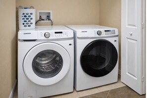 Two white Samsung front-loading washing machines in a laundry room with beige walls and a white door. - 4BR Pool Home 15 min to Disney • Heated Pool & Spa • Game Room (Kissimmee)