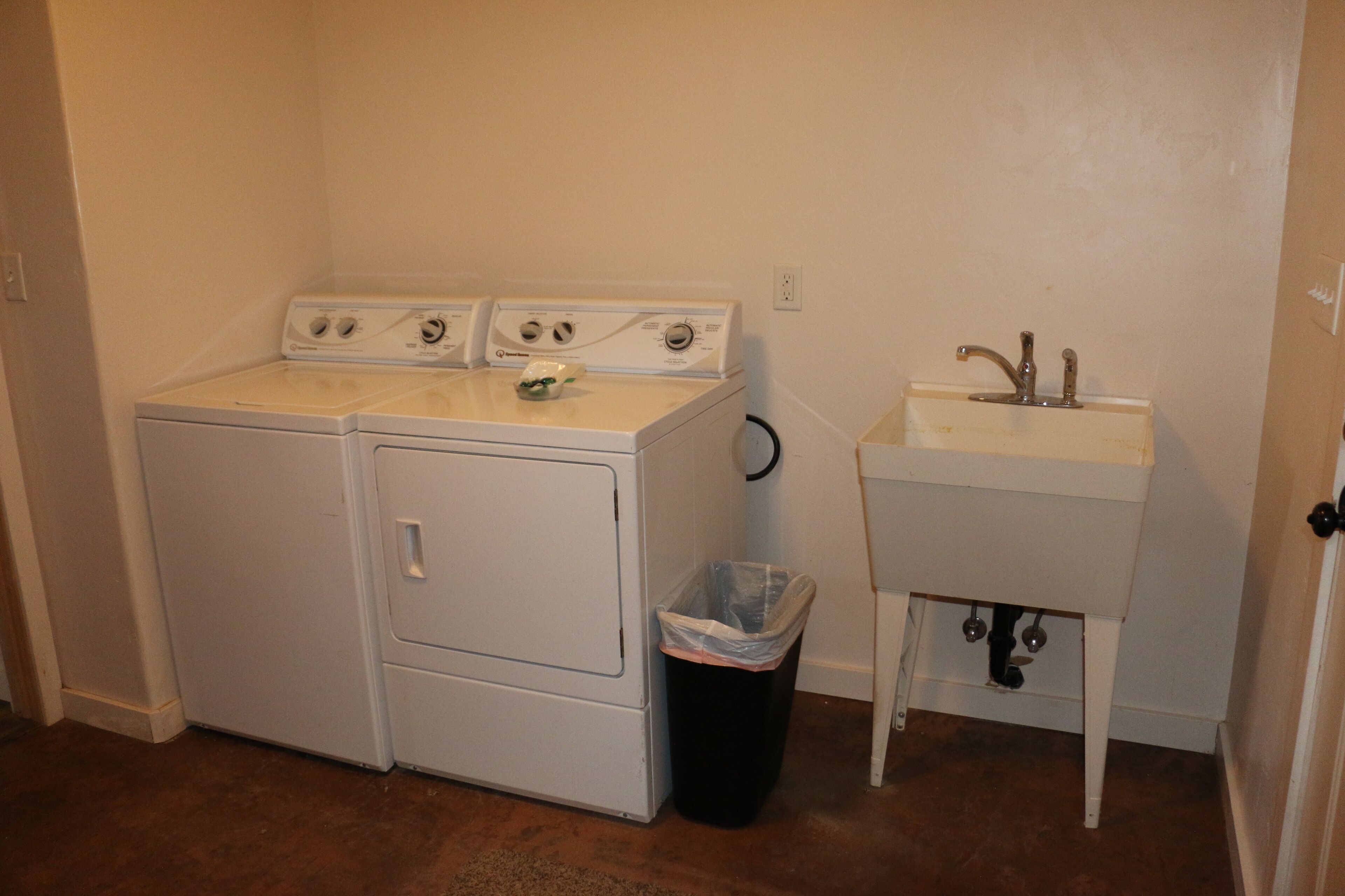 A laundry room with a washer and dryer, a sink, and a trash can.
