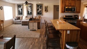 Een ruime woonkamer met een bank, een eettafel en een keuken met houten kasten en een magnetron.