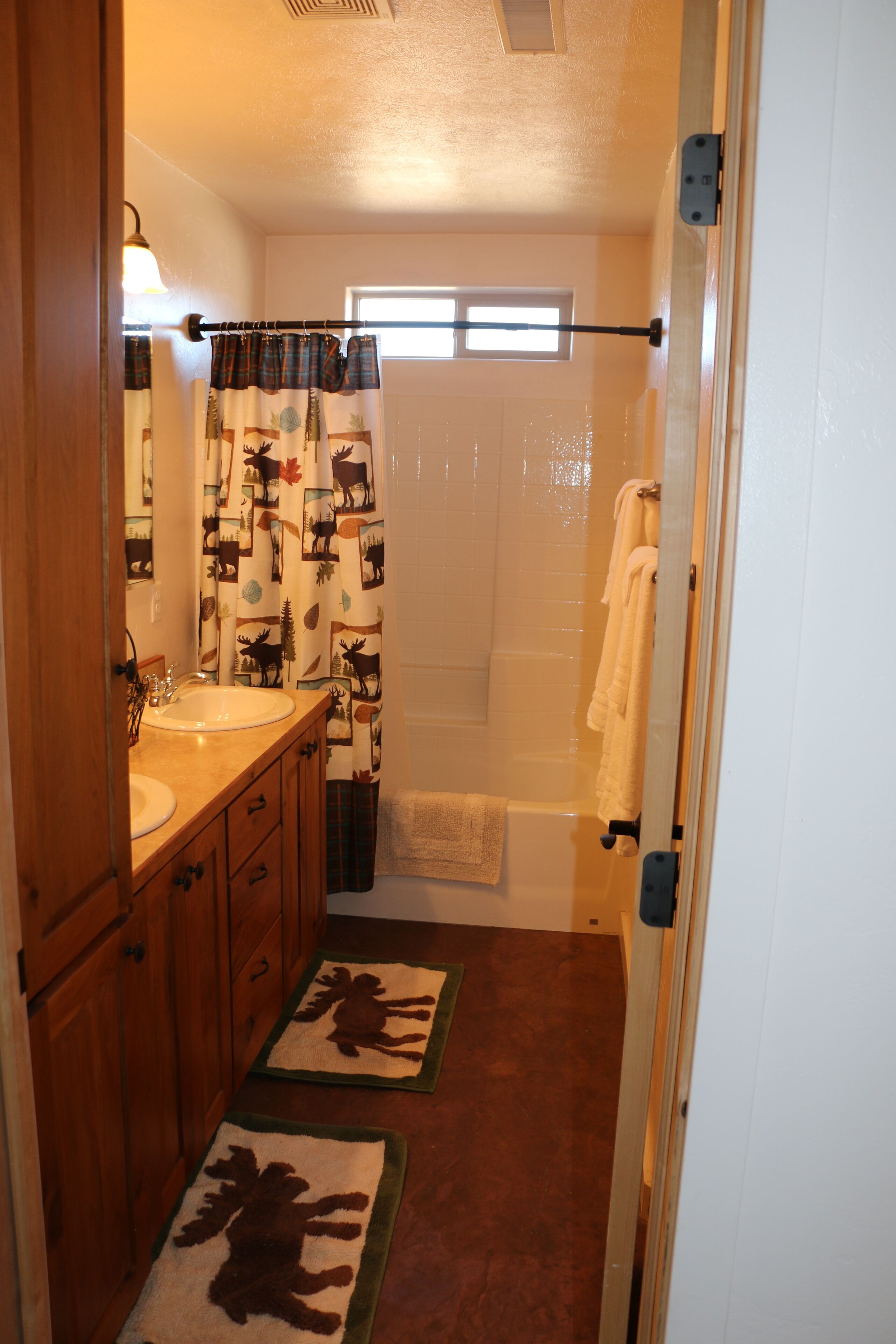 Un baño con tocador de madera, lavamanos, espejo, cortina de ducha con estampado floral y toallero.